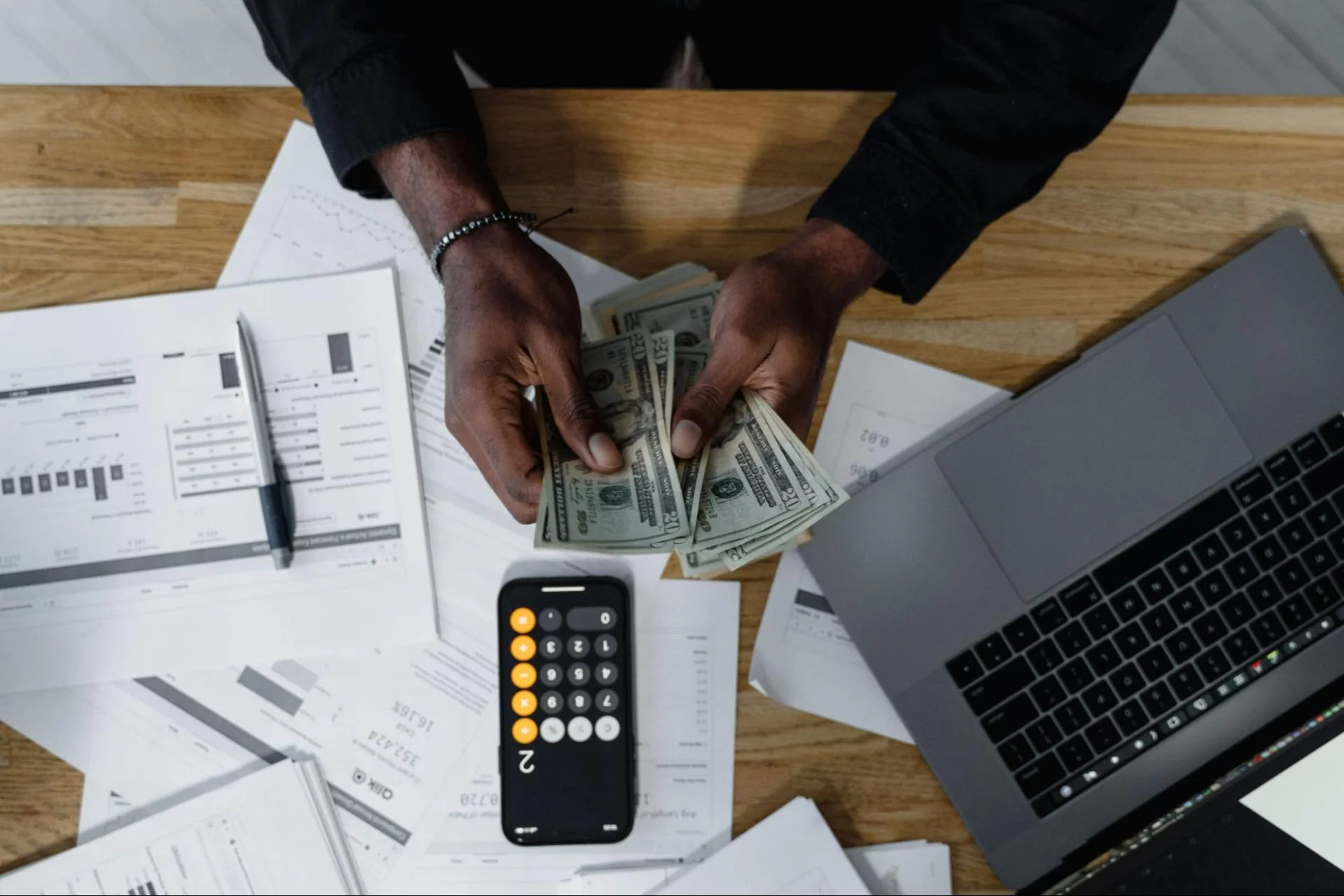 Image of a man counting cash at a desk with a calculator and spreadsheets