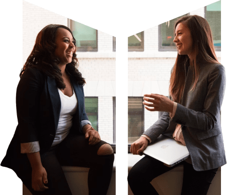 Two women sit on a ledge having an enjoyable discussion at work